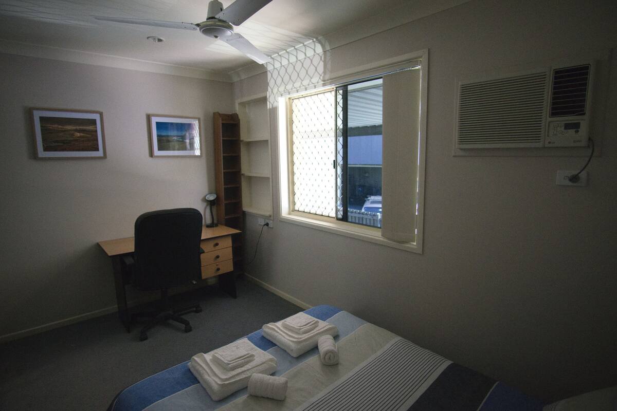 A bedroom with a bed, a desk, a chair, and a window with blinds.