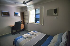 Une chambre à coucher comprenant un lit, un bureau, une chaise, une fenêtre et un appareil de climatisation.