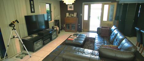 A living room with a large leather sofa, a flat-screen TV, a tripod, and a cabinet.