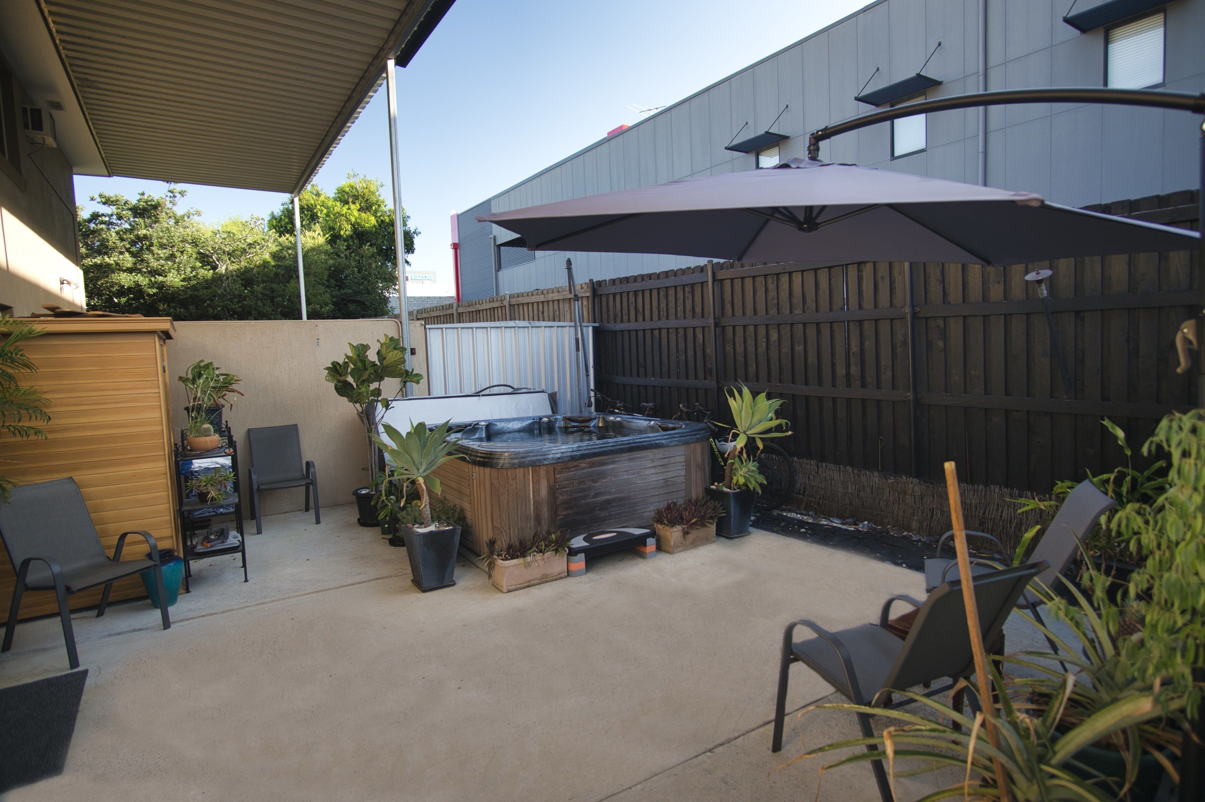 Een achtertuin met een hottub, terrasstoelen, planten in potten en een houten omheining.