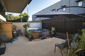 Un jardin avec un jacuzzi, des chaises de patio, des plantes en pot et une clôture en bois.