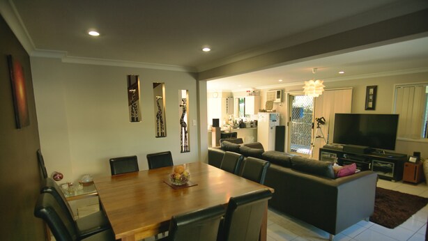 A modern living room with a dining area, a sofa, a TV, and a kitchen in the background. - Mount Gravatt Guesthouse (Mount Gravatt East)