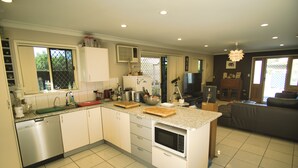 A modern kitchen with a central island, built-in appliances, and a dining area with a couch. - Mount Gravatt Guesthouse (Mount Gravatt East)