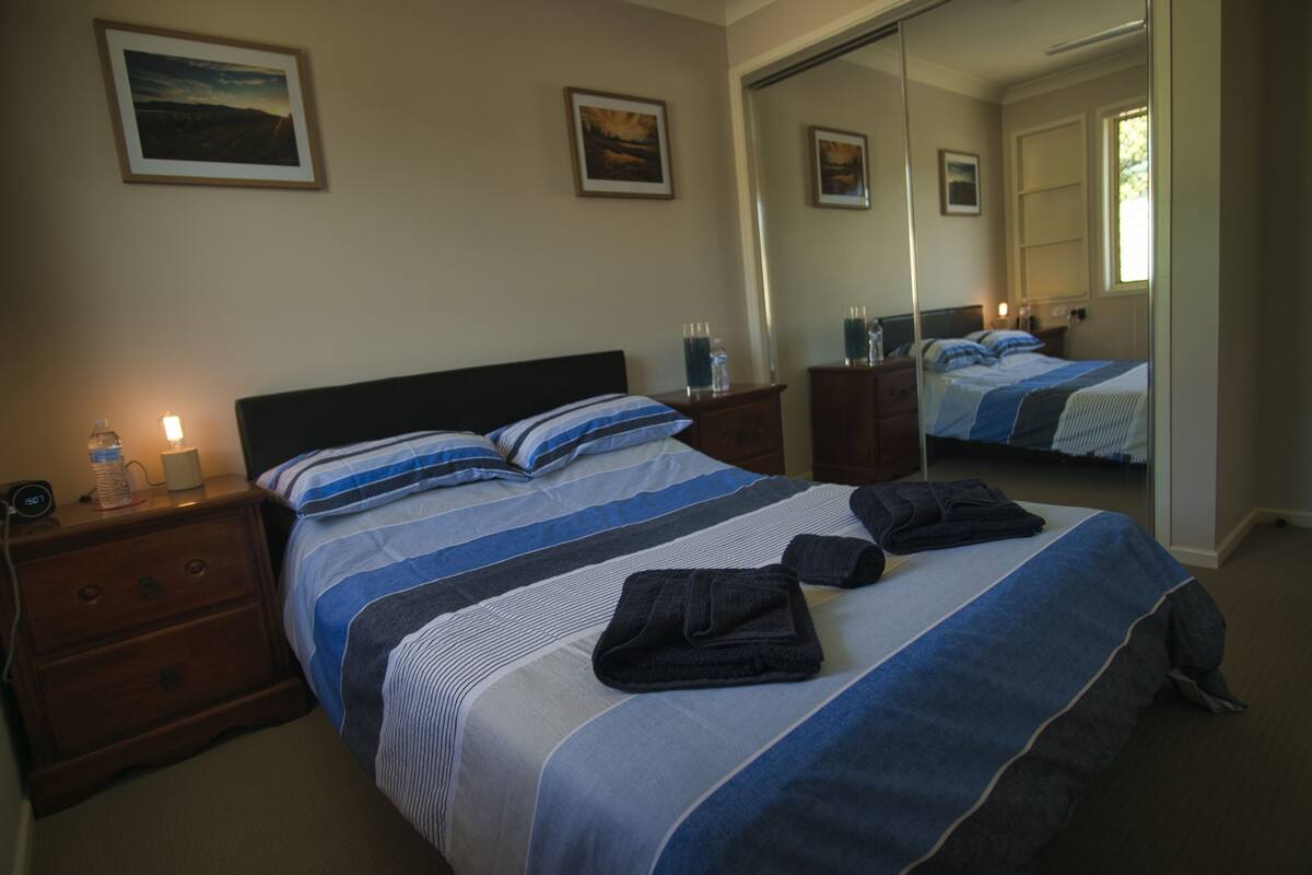 A neatly made bed with striped bedding, a bedside table with a lamp, and a mirror reflecting the room.