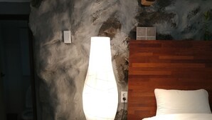 Un dormitorio con pared de piedra, cabecera de madera, cama blanca y una lámpara de pie.
