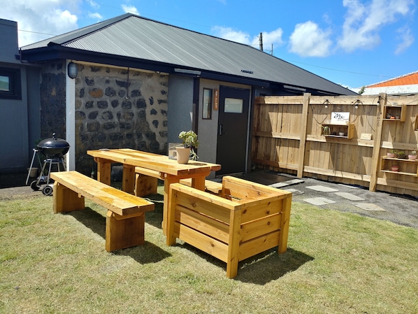 A patio with wooden furniture, a barbecue grill, and a stone wall.