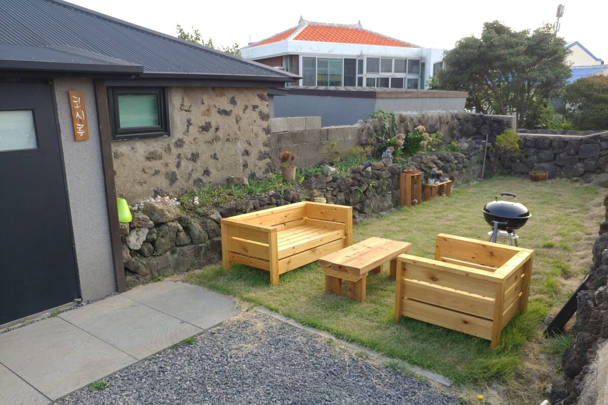 Un patio trasero con muro de piedra, mobiliario de madera y una parrilla.