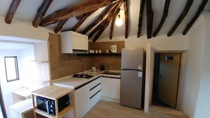Una cocina compacta con vigas de madera, estufa integrada, refrigerador y gabinetes blancos.