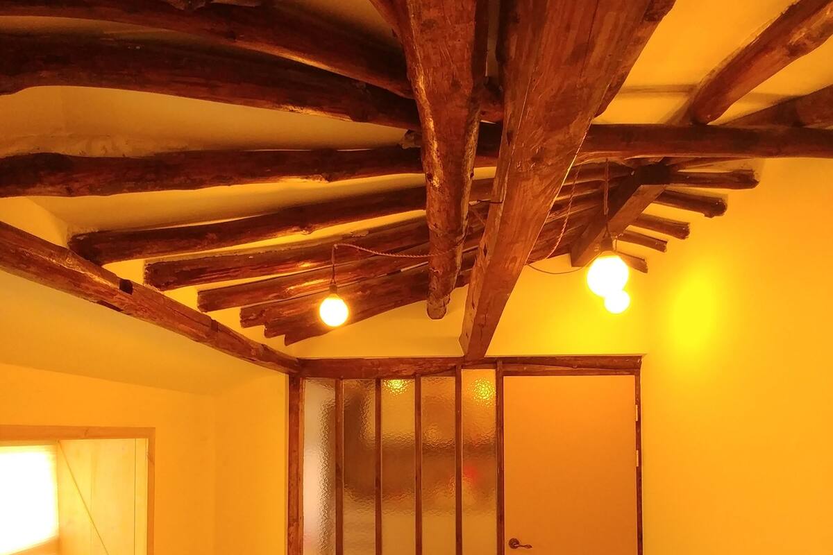 Una habitación con cama, vigas de madera, una puerta de cristal esmerilado y una ventana.