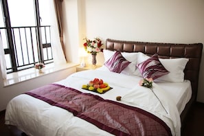 A neatly made bed with a fruit basket, pillows, and a vase of flowers on a nightstand.