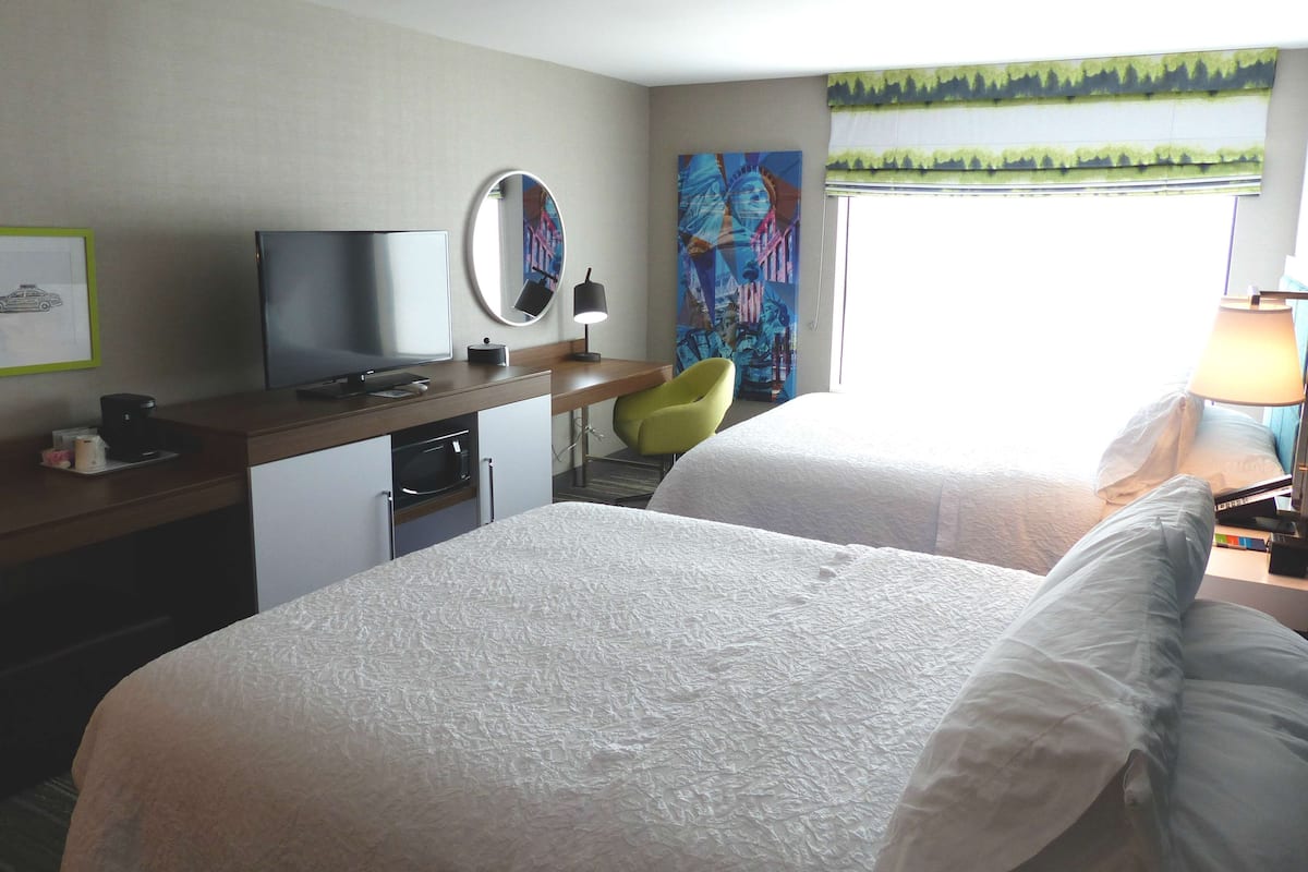 A hotel room with two beds, a desk with a TV, a chair, and artwork on the wall.
