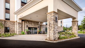 A hotel entrance with a covered walkway, stone pillars, and a 'Welcome' sign.