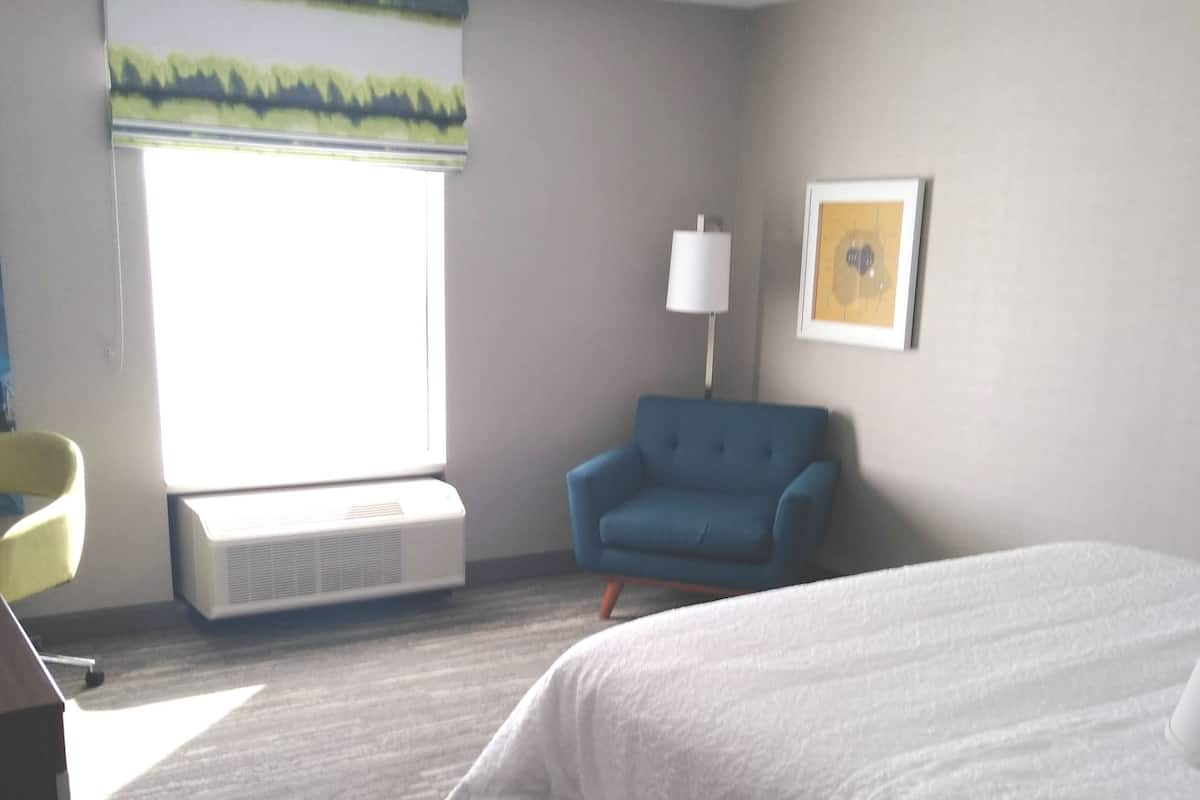 A hotel room with a bed, a chair, a desk, a lamp, and a window with a view.