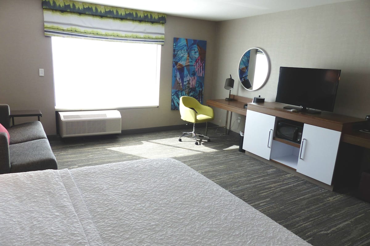 A hotel room with a bed, a desk, a chair, a television, and a painting on the wall.