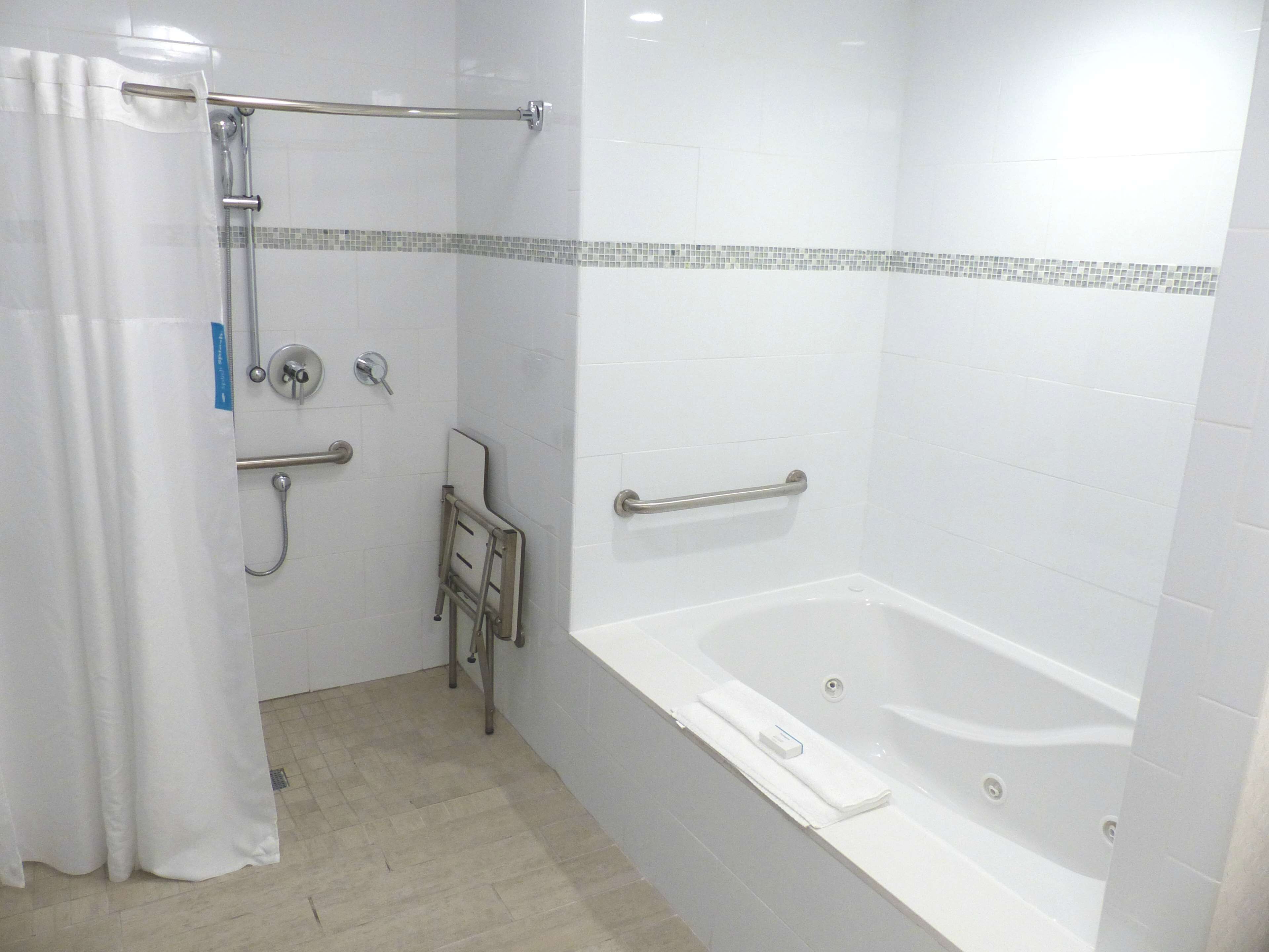 A modern bathroom with a bathtub, shower, and handrails.