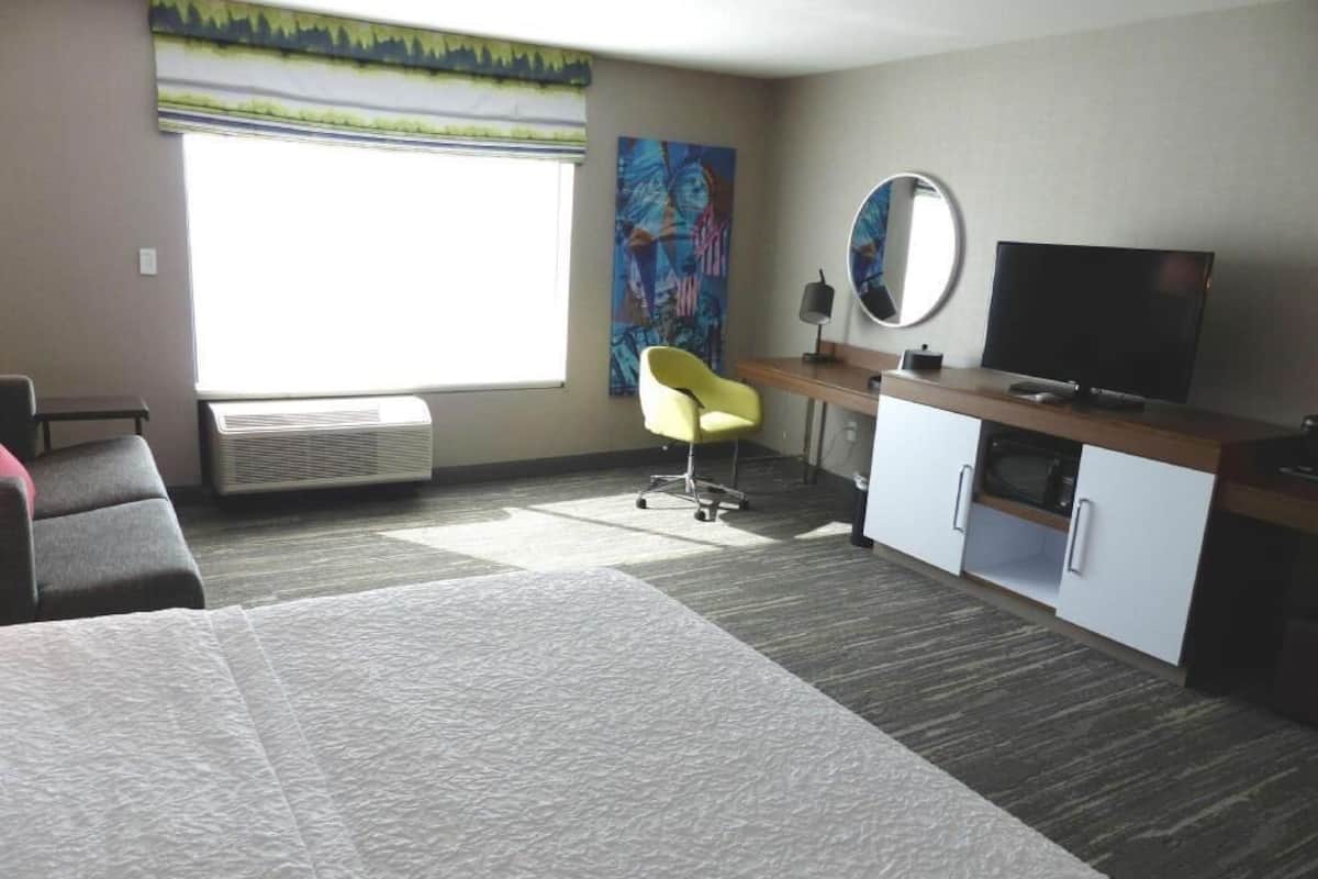 A hotel room with a bed, a desk, a chair, a TV, and a large window.