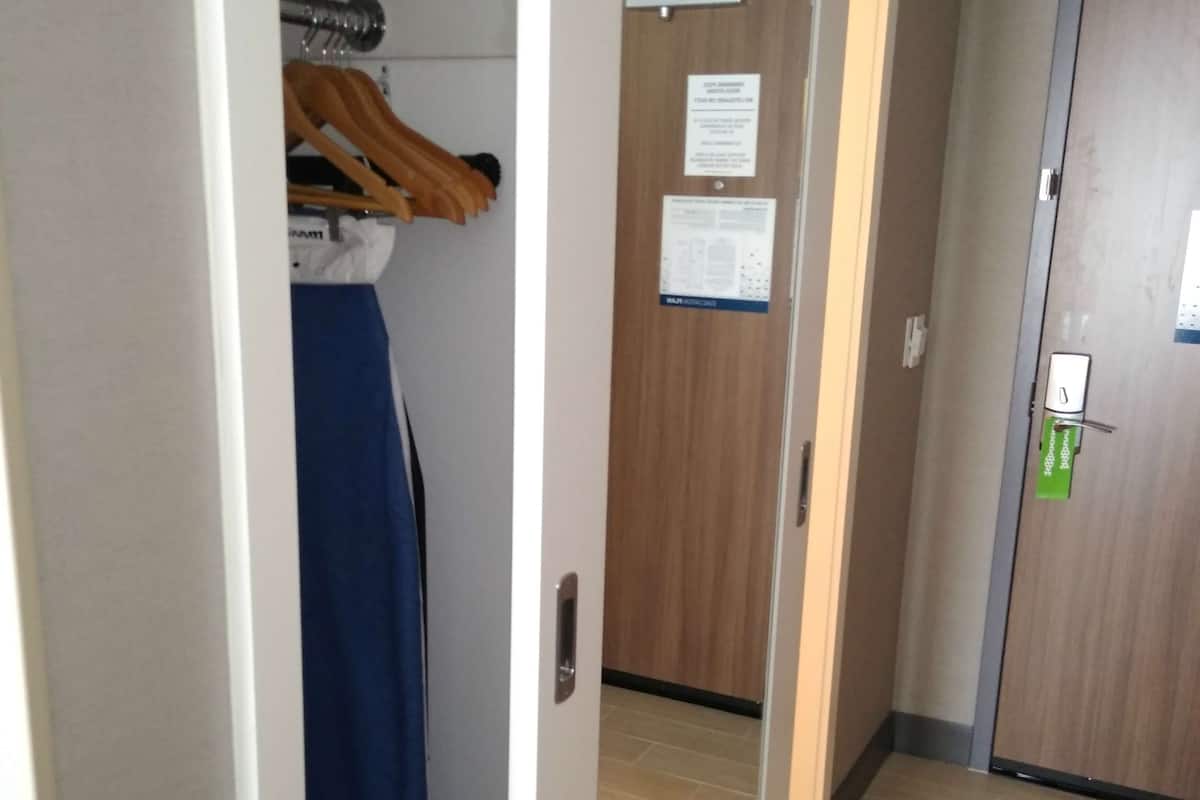 A hallway with a wooden floor, a mirror on the wall, and a door with a green lock.