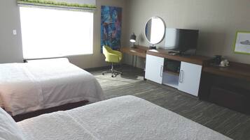 Habitación de hotel con dos camas, un escritorio con televisor, una silla y un cuadro en la pared.