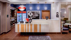 A hotel reception area with a counter, a 'Treats' sign, a 'Enjoy' poster, and a 'Making You Happy Makes Us Happy' mat.