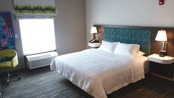 A hotel room with a large bed, two bedside tables with lamps, a chair, and a window with blinds.