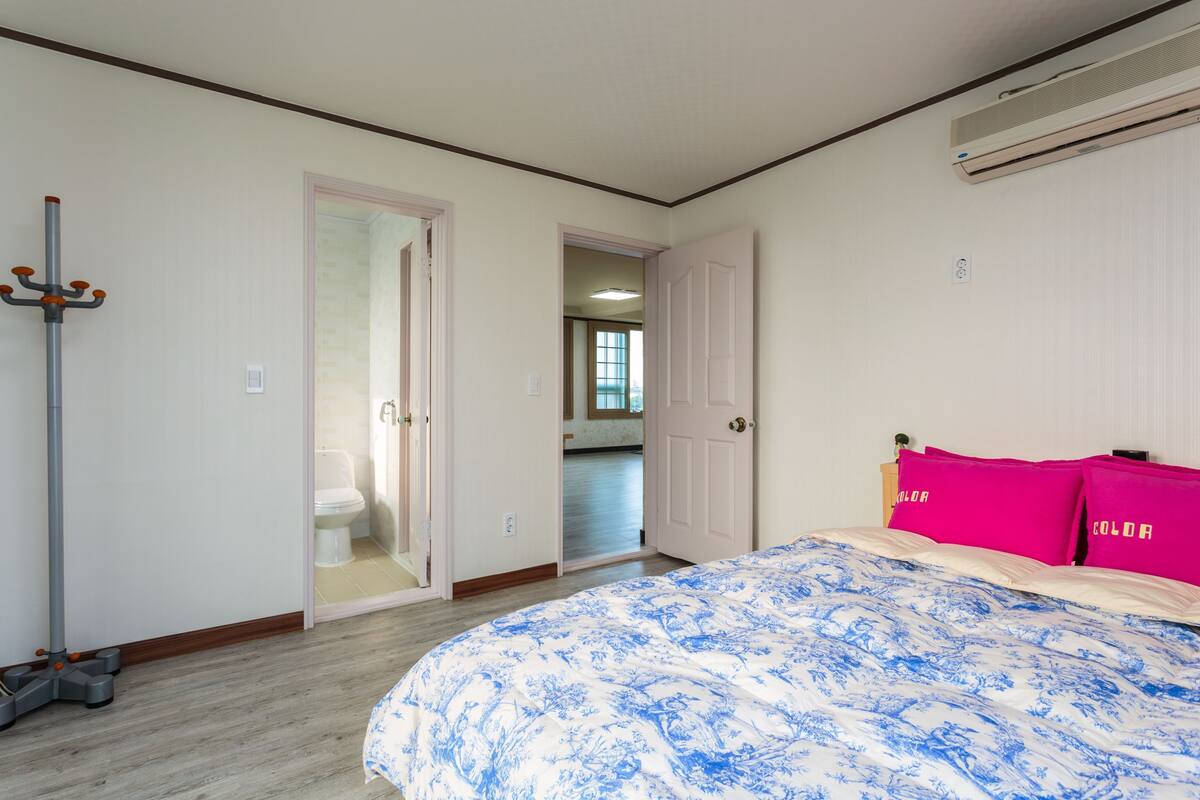 Une chambre à coucher avec un lit, une porte donnant sur une salle de bain et un appareil de climatisation fixé au mur.