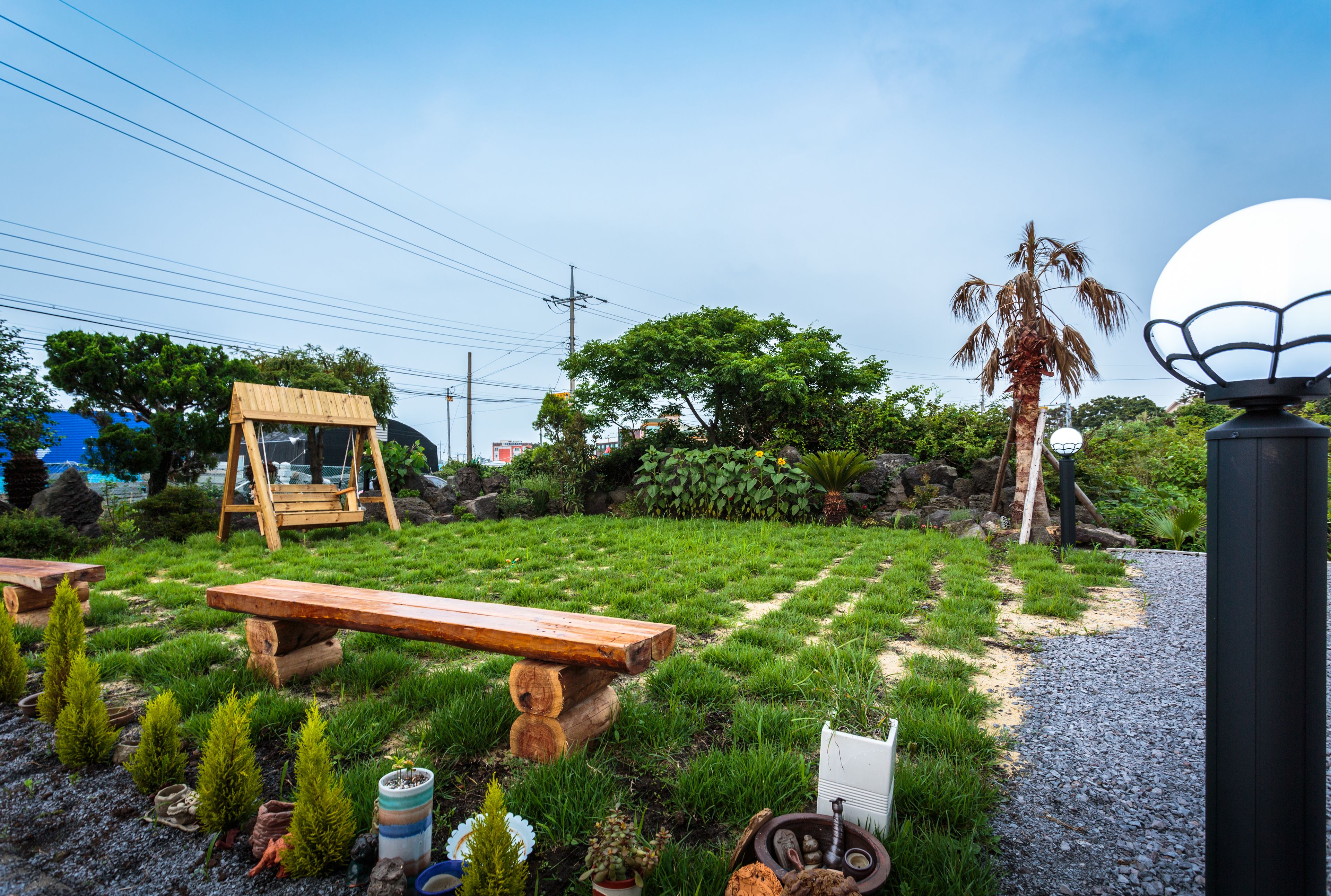 Un jardín con un columpio de madera, un banco y un sendero que lleva a una palmera.