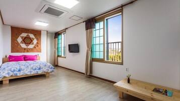 Ein Schlafzimmer mit einem Bett, einer hölzernen Bank, einem Fernseher und großen Fenstern.
