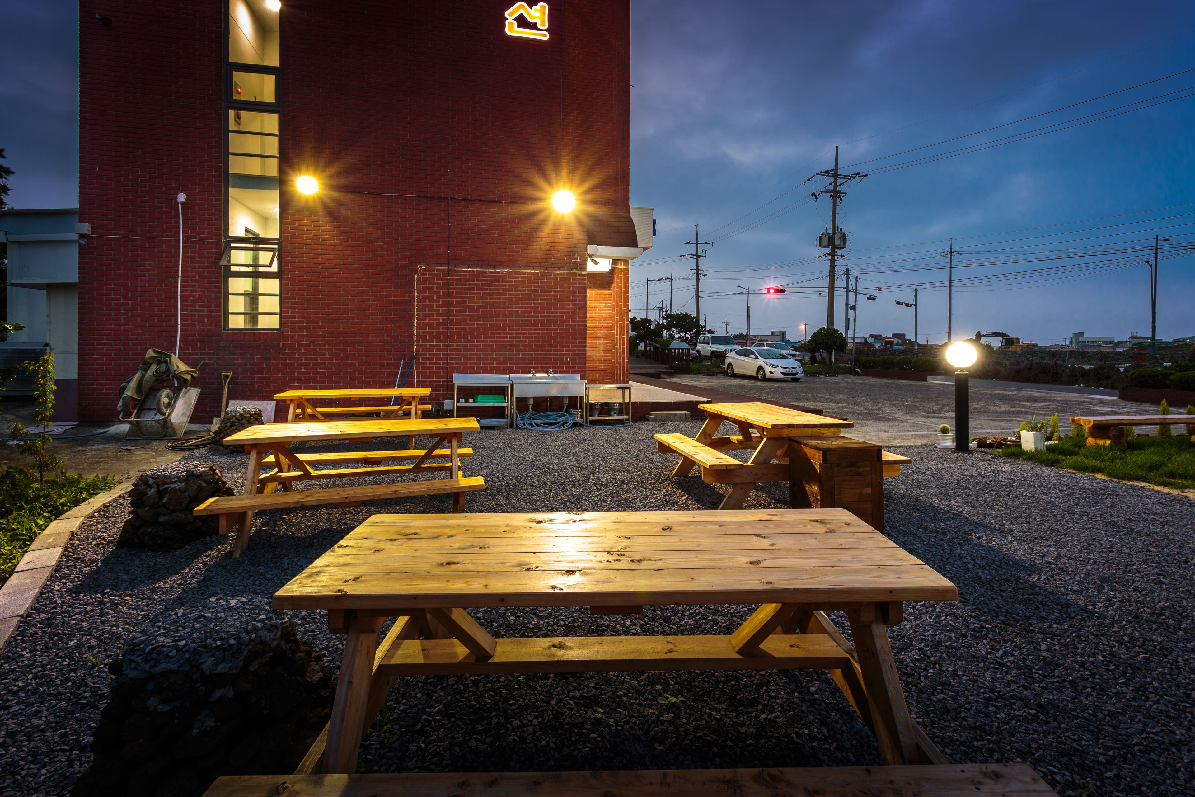 A building with a red brick exterior and multiple wooden picnic tables arranged in front.
