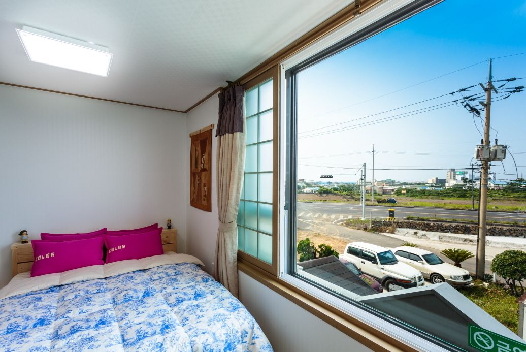 Habitación de hotel con un ventanal grande, una cama con colcha de diseño azul y blanco, y dos almohadas rosas.