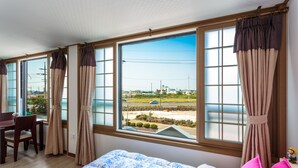 Un dormitorio con una cama, un escritorio y una silla. Hay ventanas grandes con cortinas.