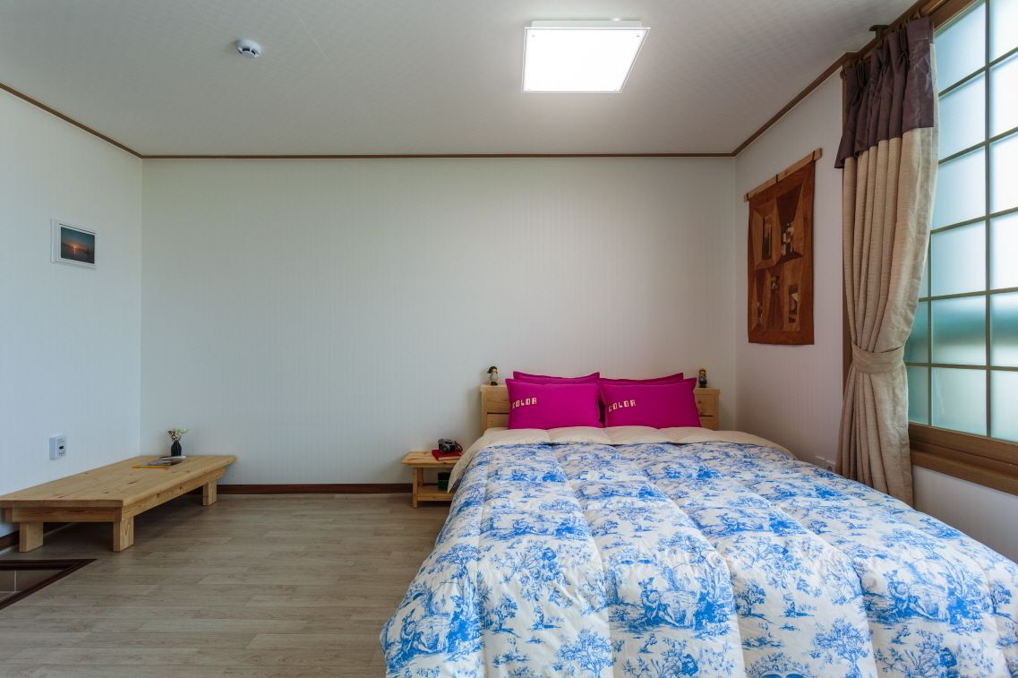 Un dormitorio con cama, mesita de noche, banco de madera y ventana con cortinas.