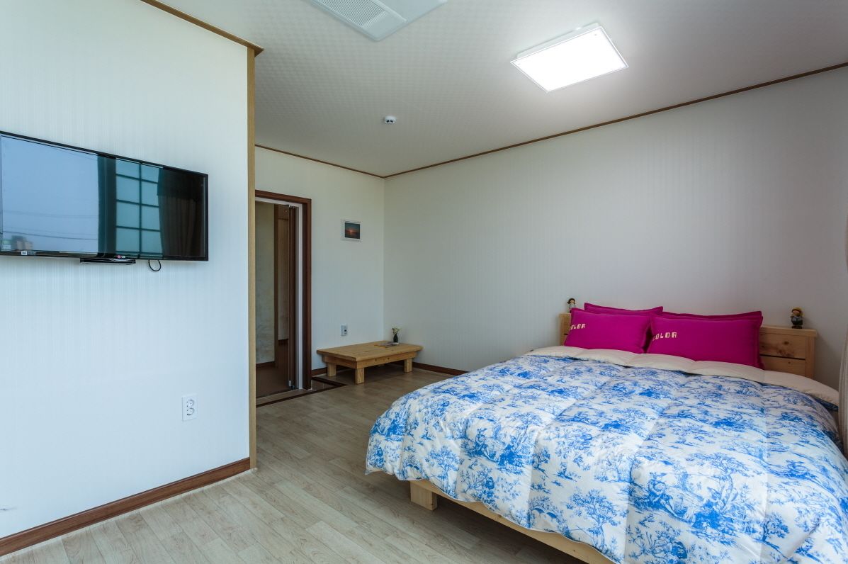 A bedroom with a bed, a TV mounted on the wall, a wooden bench, and a door leading to another room.
