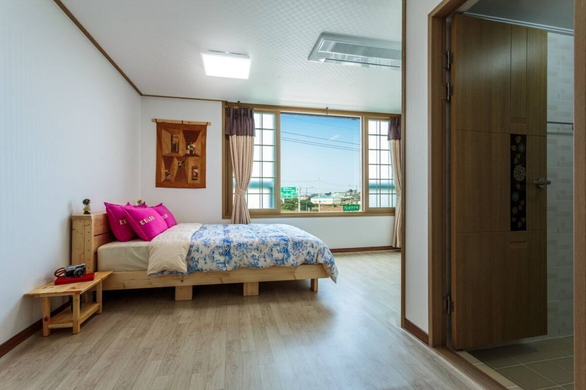 Une chambre à coucher avec un lit, une table de chevet en bois, une fenêtre avec des rideaux et une armoire.