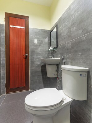A bathroom with a wooden door, a white toilet, a sink, and a mirror on the wall. - Vaccinated Staff - OYO 567 Blue Horizon Hostel (Dumaguete)