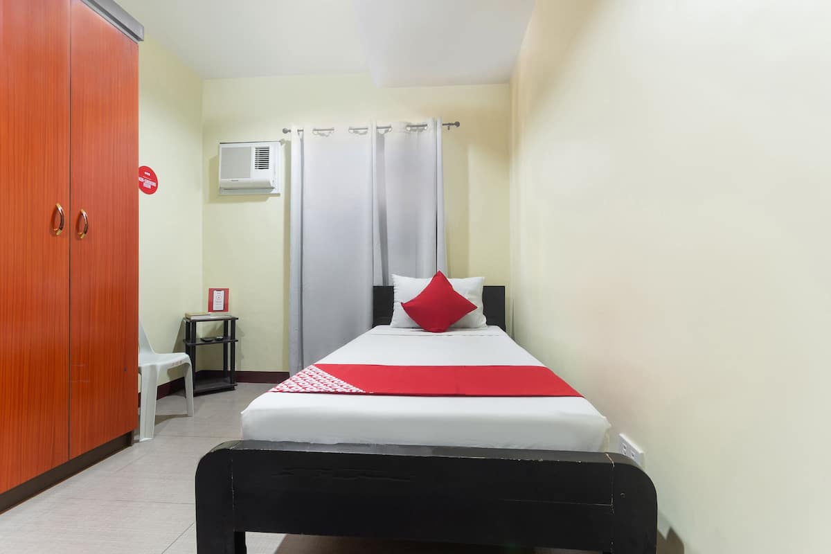 A hotel room with a bed, a wardrobe, a small table, and an air conditioning unit.