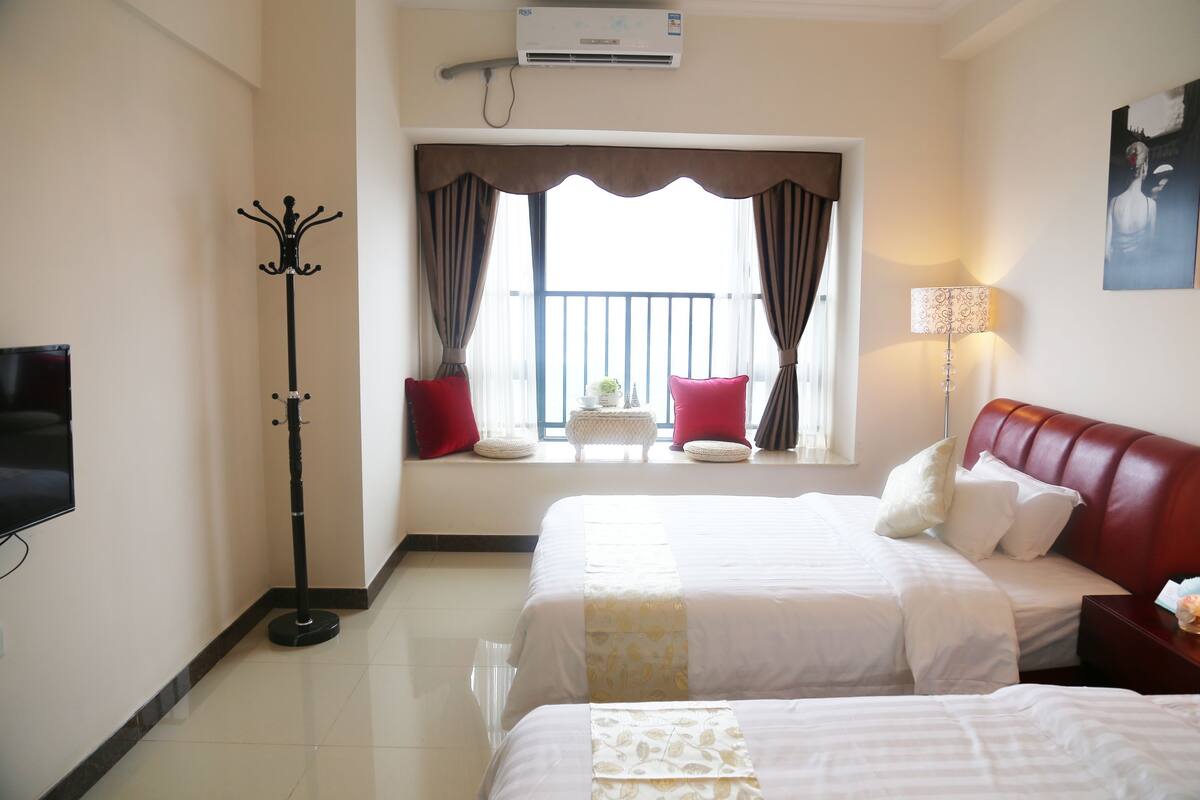 Habitación de hotel con dos camas, un televisor, perchero, ventana con cortinas y aire acondicionado de pared.