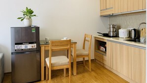 Een kleine keuken met een koelkast, een eettafel met stoelen, houten kastjes en een aanrecht met diverse keukenapparaten.