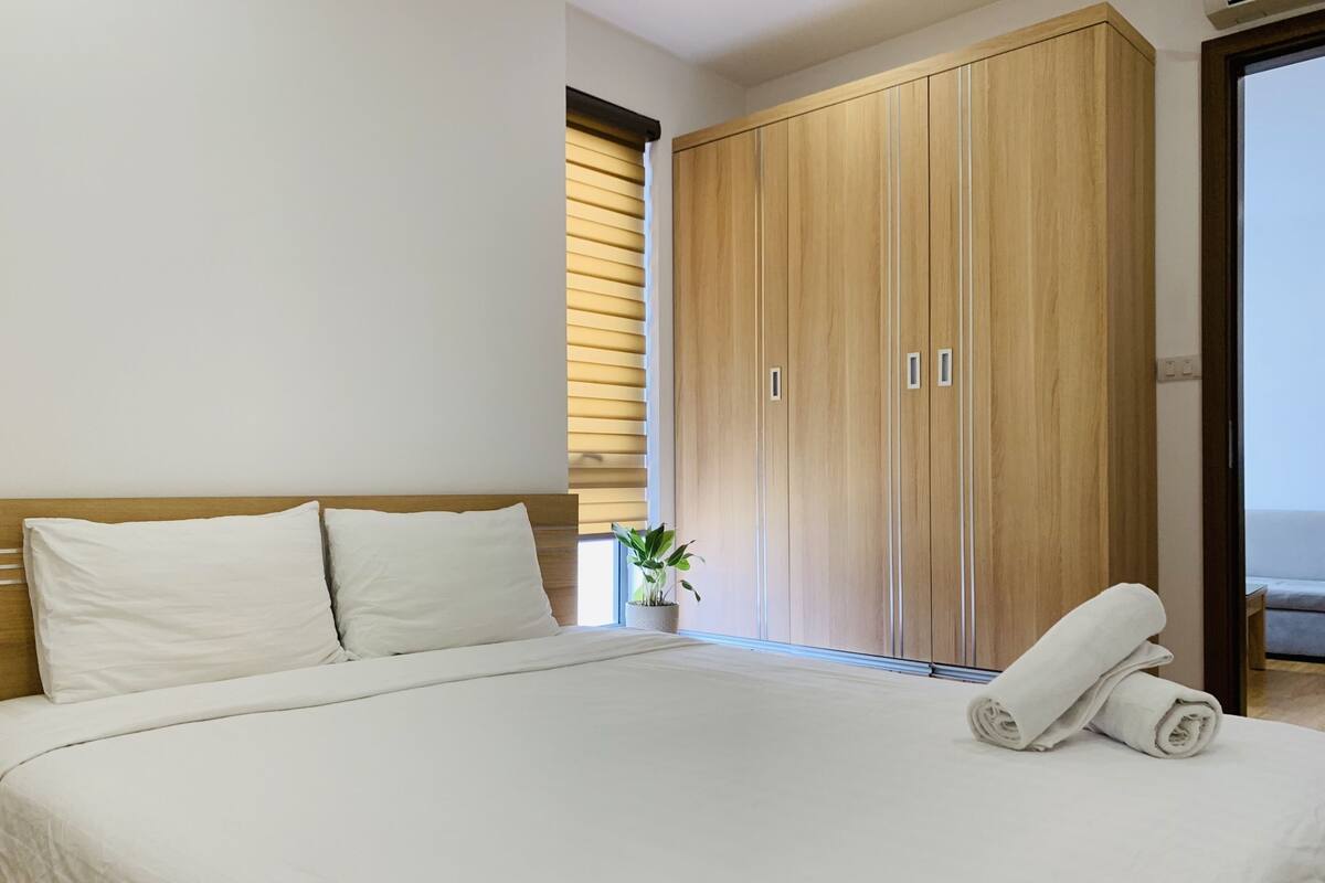 A bedroom with a large bed, wooden wardrobe, and a potted plant.
