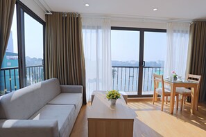 A modern living room with a sofa, a glass-top dining table, and a view of a cityscape through large windows. - Nythome Truc Bach (Hanoi)