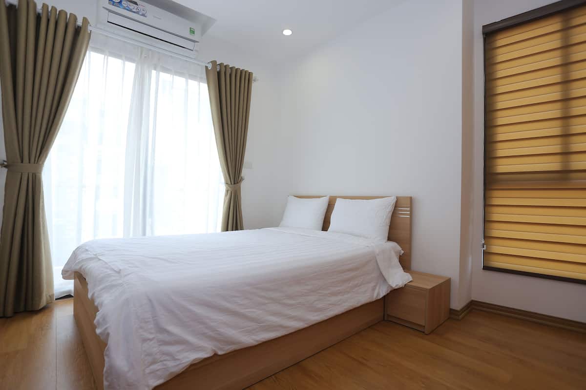 A bedroom with a wooden bed, white bedding, and a window with curtains.