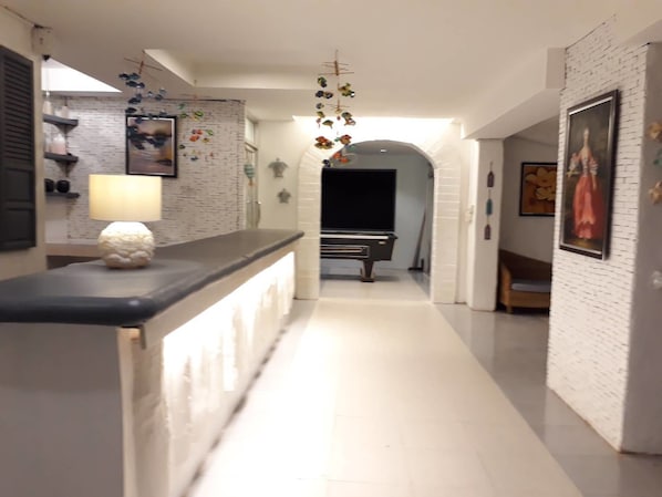 A hallway with a white brick wall, a black counter with a white lamp, and a TV in the background.