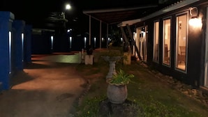 A nighttime view of a building with a covered patio area, a potted plant, and a pathway leading to the entrance. - Sea Turtle Hostel - Adults Only (Ko Chang)