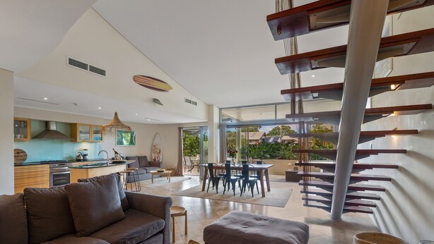 A modern living room with a sofa, ottoman, and a dining area with a table and chairs. - Jades on Lawson 2 (Byron Bay)