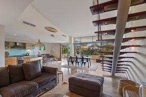 A modern living room with a sofa, ottoman, and a dining area with a table and chairs. - Jades on Lawson 2 (Byron Bay)