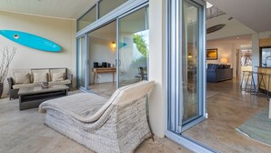 A modern living area with a wicker sofa, a glass sliding door, and a surfboard on the wall. - Jades on Lawson 2 (Byron Bay)