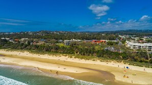 A coastal town with a sandy beach, clear skies, and residential buildings in the background. - Jades on Lawson 2 (Byron Bay)