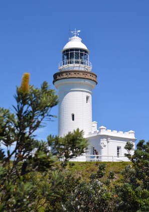 A lighthouse with a white cylindrical tower and a dome on top, surrounded by greenery. - Jades on Lawson 2 (Byron Bay)