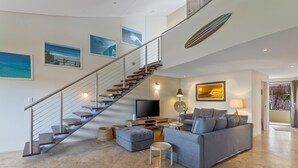 A spacious living area with a staircase, a sofa, a television, and artwork on the walls. - Jades on Lawson 2 (Byron Bay)