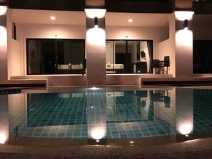 Une piscine dont le fond est recouvert de carrelage, entourée d’un bâtiment doté de grandes fenêtres et d’un espace aménagé avec des sièges.