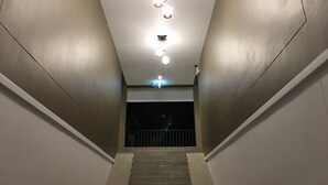 Eine Treppe führt zu einem dunklen Bereich mit einer Überwachungskamera und Deckenleuchten.